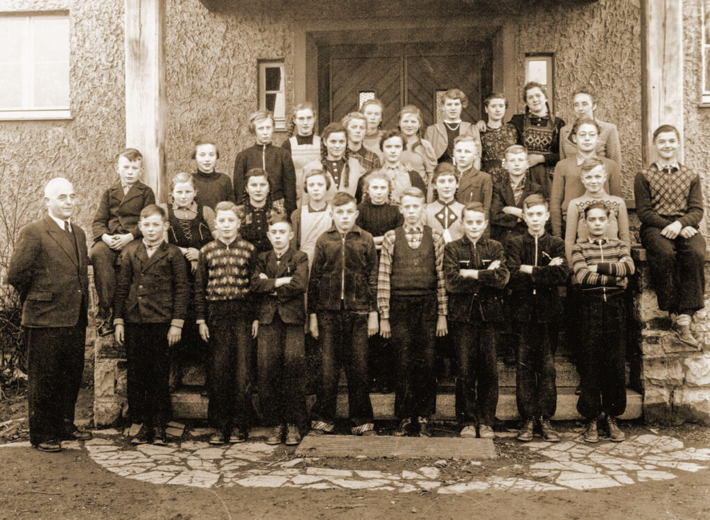 Eine Gruppe Kinder steht mit ihrem Lehrer vor einem Gebäude